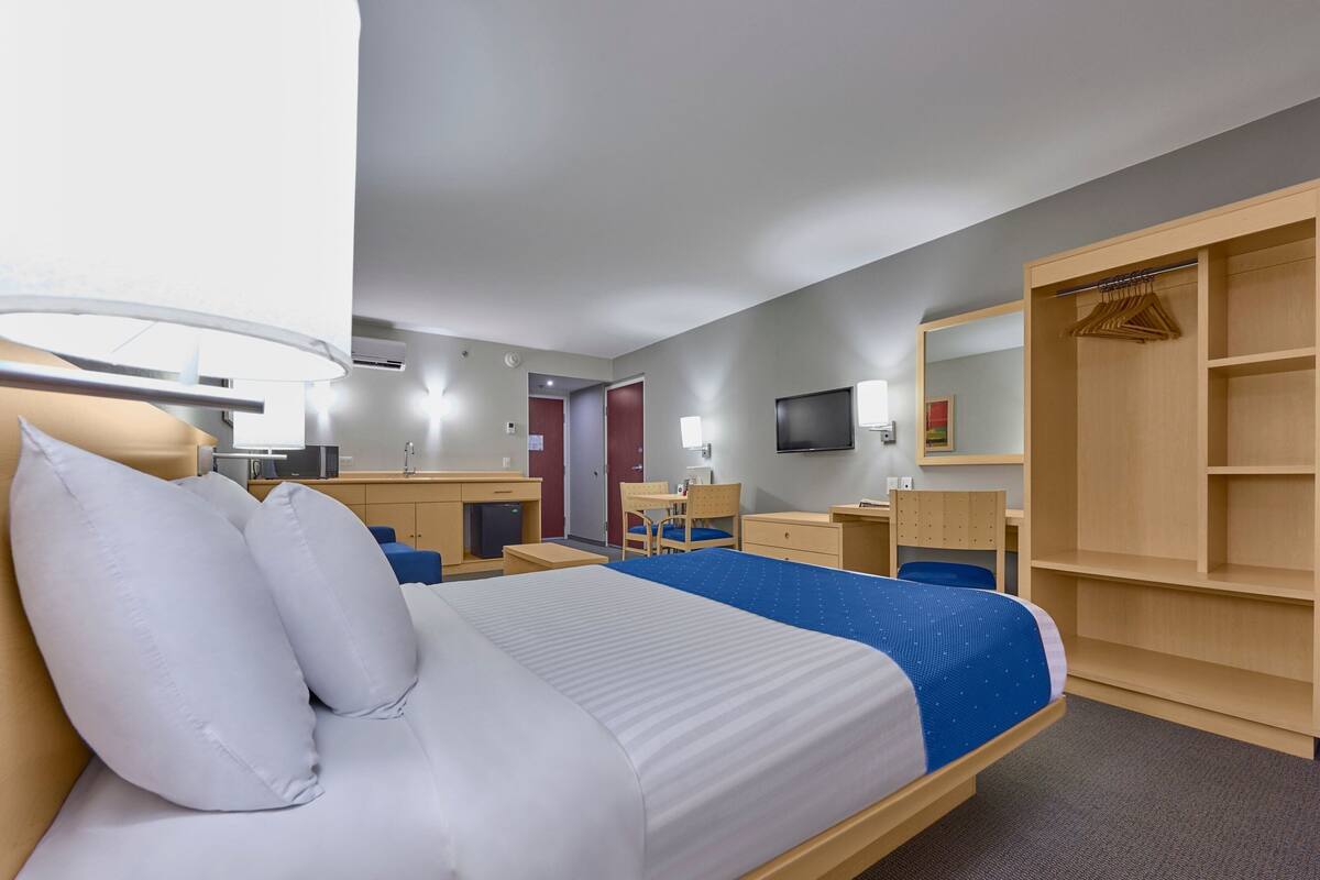 Habitación de hotel con cama, mesita de noche, escritorio, silla, armario y televisor.