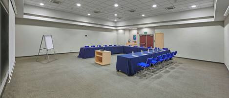 A large conference room with a long table, blue chairs, a whiteboard, and a small wooden cabinet.