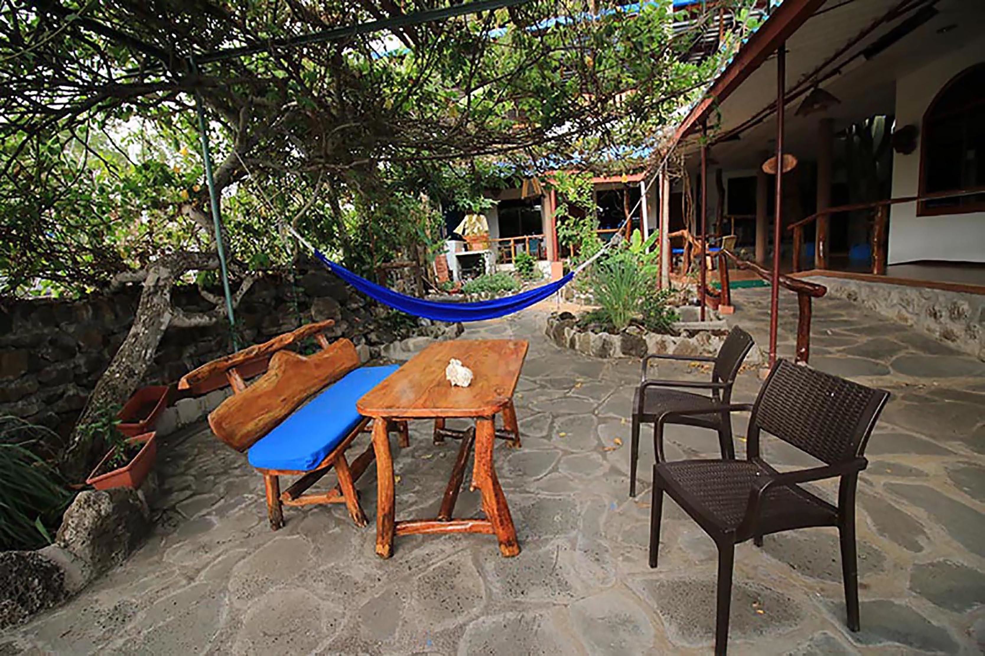 An outdoor patio with a wooden table and chairs, a hammock, and a stone floor.