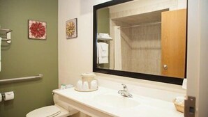 Une salle de bain avec un lavabo blanc, un miroir et des toilettes. Deux éléments décoratifs ornent les murs, l’un est rouge et l’autre est doré.