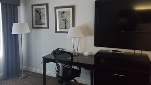 Une chambre d’hôtel équipée d’un bureau, de deux lampes, d’une télévision et de deux tableaux encadrés accrochés au mur.