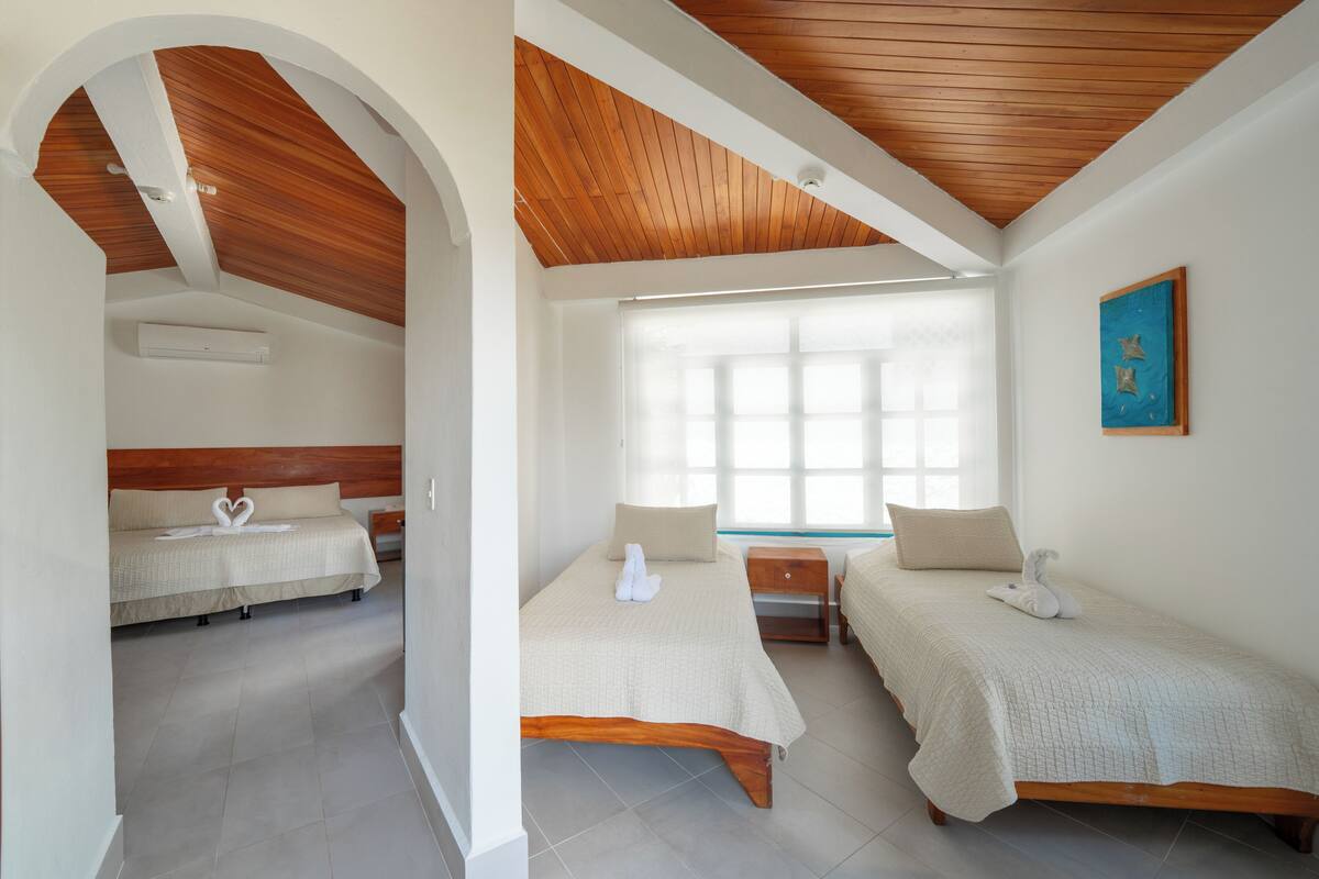 A hotel room with two beds, wooden ceiling beams, a large window, and a painting on the wall.