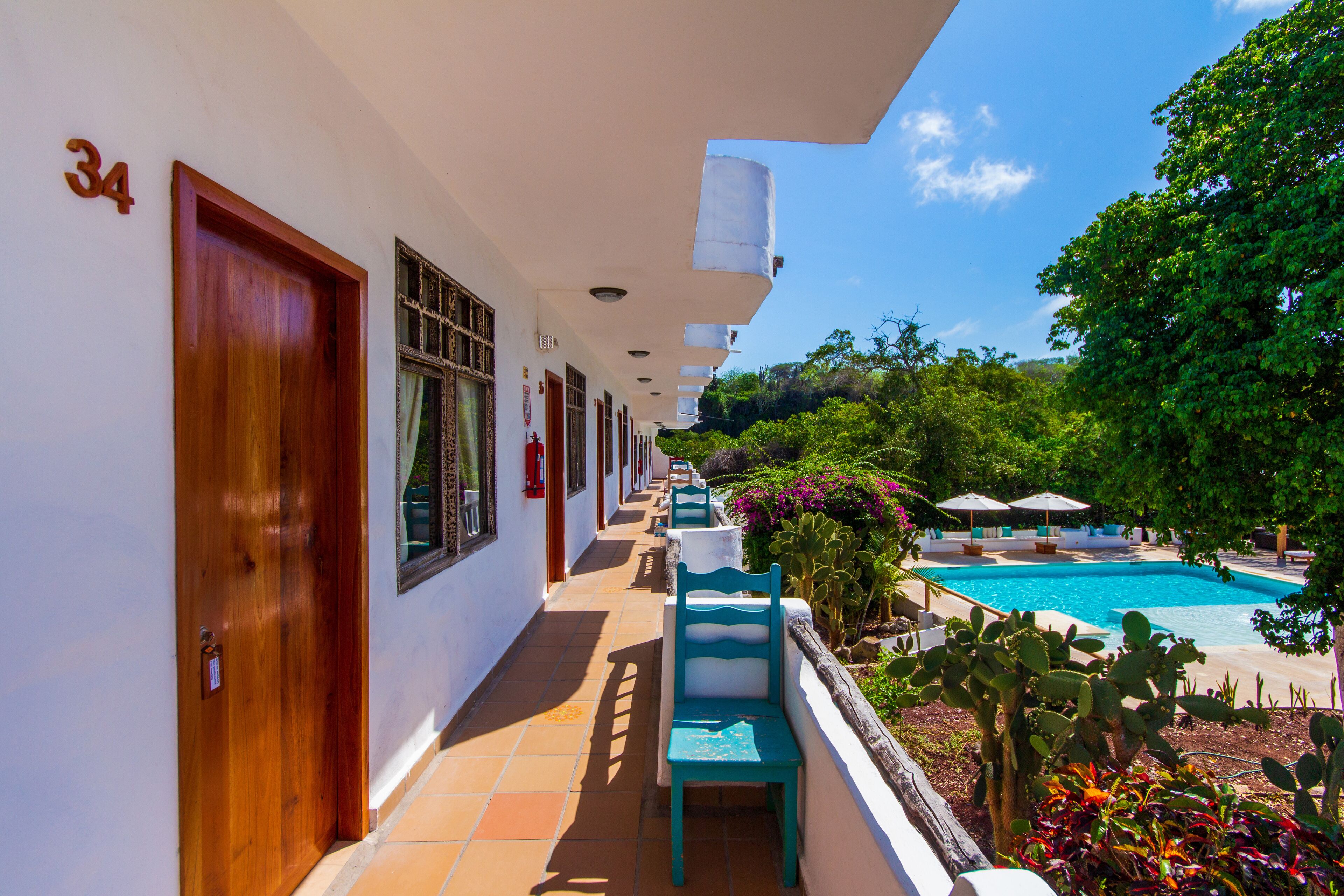 A hotel corridor with a pool, outdoor seating, and greenery.