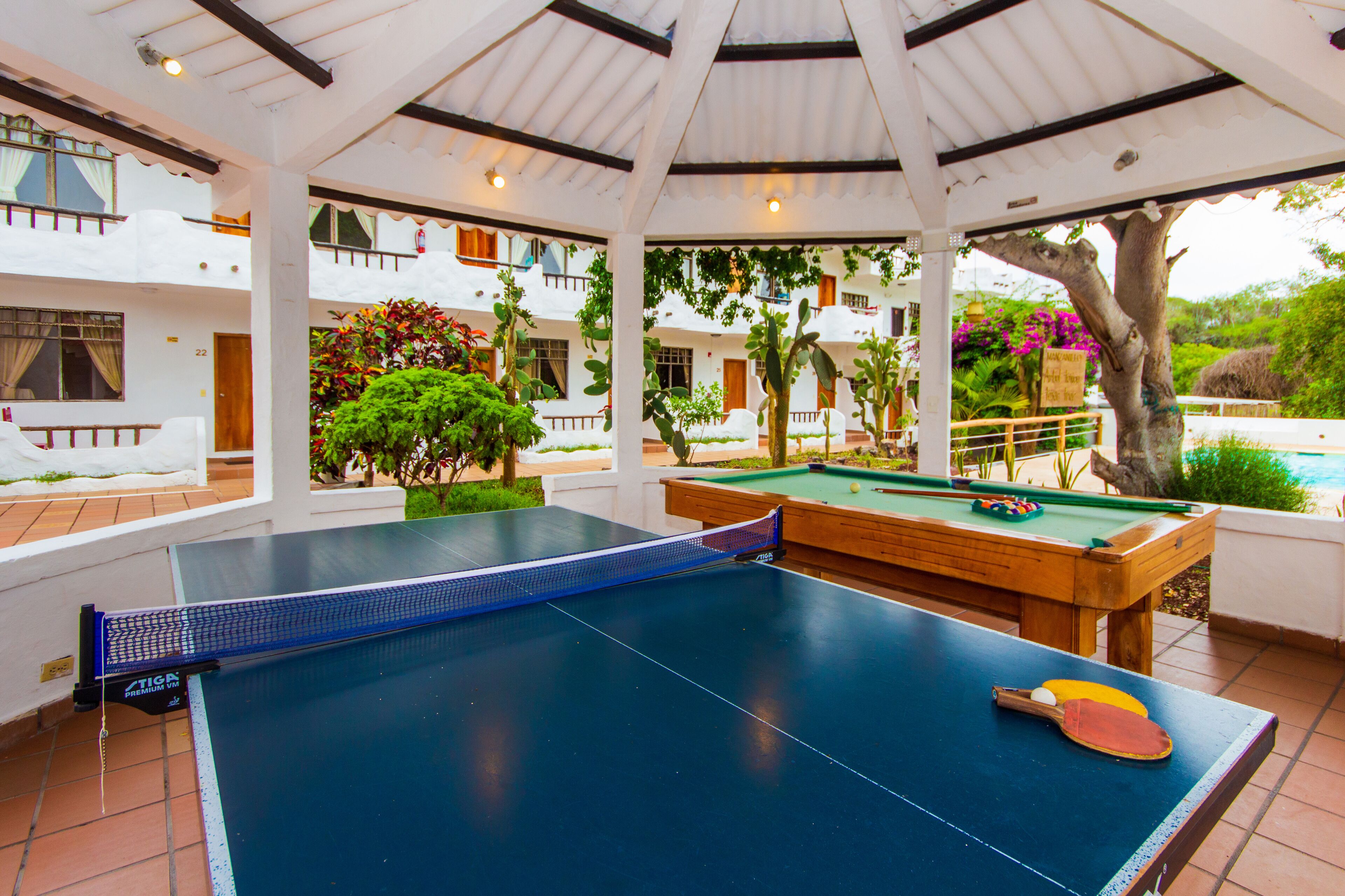 Una mesa de ping pong en un espacio exterior cubierto, con una mesa de billar cerca.