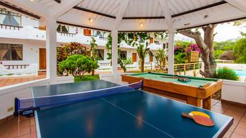 Una mesa de ping pong en un espacio exterior cubierto, con una mesa de billar cerca.