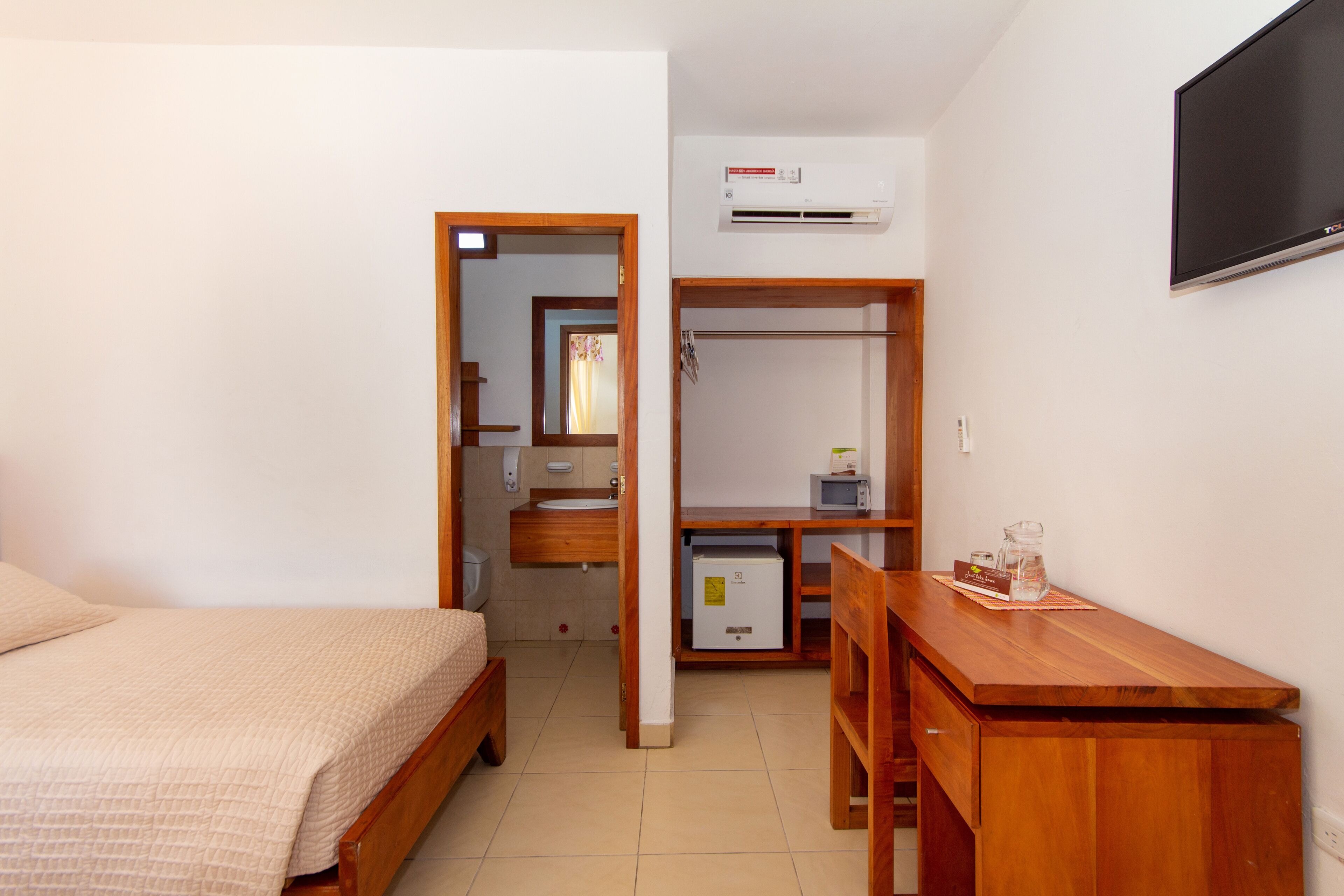 A bedroom with a bed, a wooden desk, a television, and an air conditioning unit.