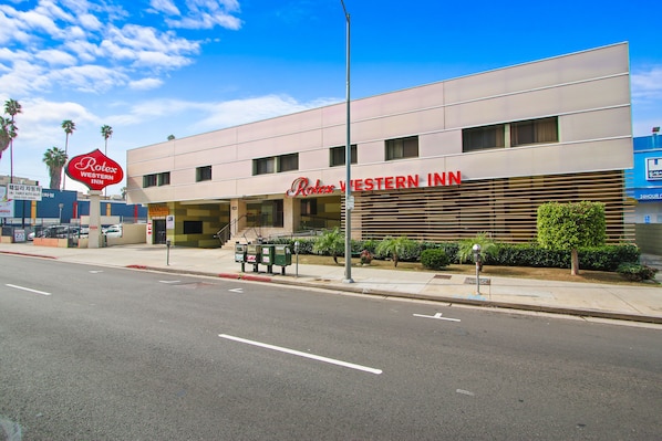 Situated on a street corner, the Rolex Western Inn features a modern architectural design with a prominent sign and neutral facade.