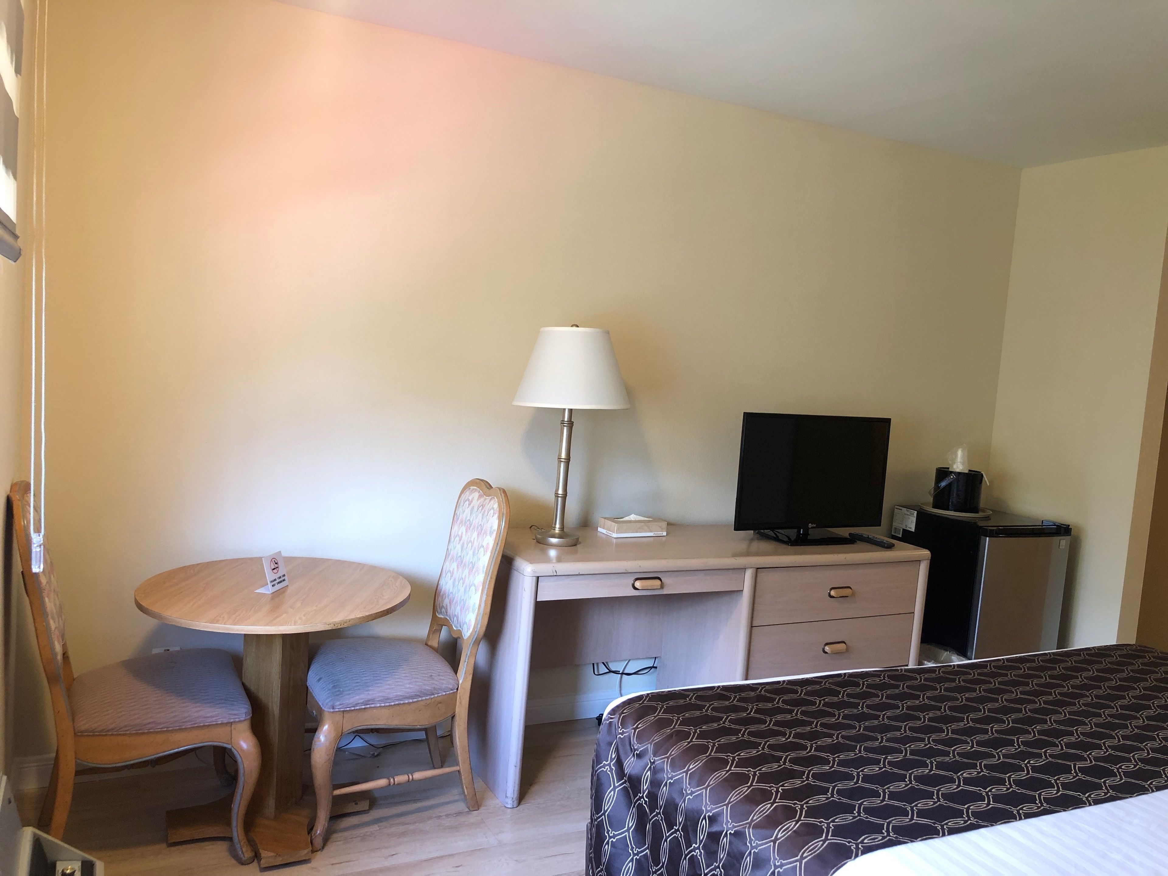 A hotel room with a bed, a desk with a chair, a television, and a lamp.