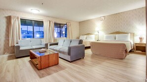 A hotel room with a sofa, a small table, a bed with a patterned bedspread, a nightstand, and a window with curtains. - Rotex Western Inn (Los Angeles)