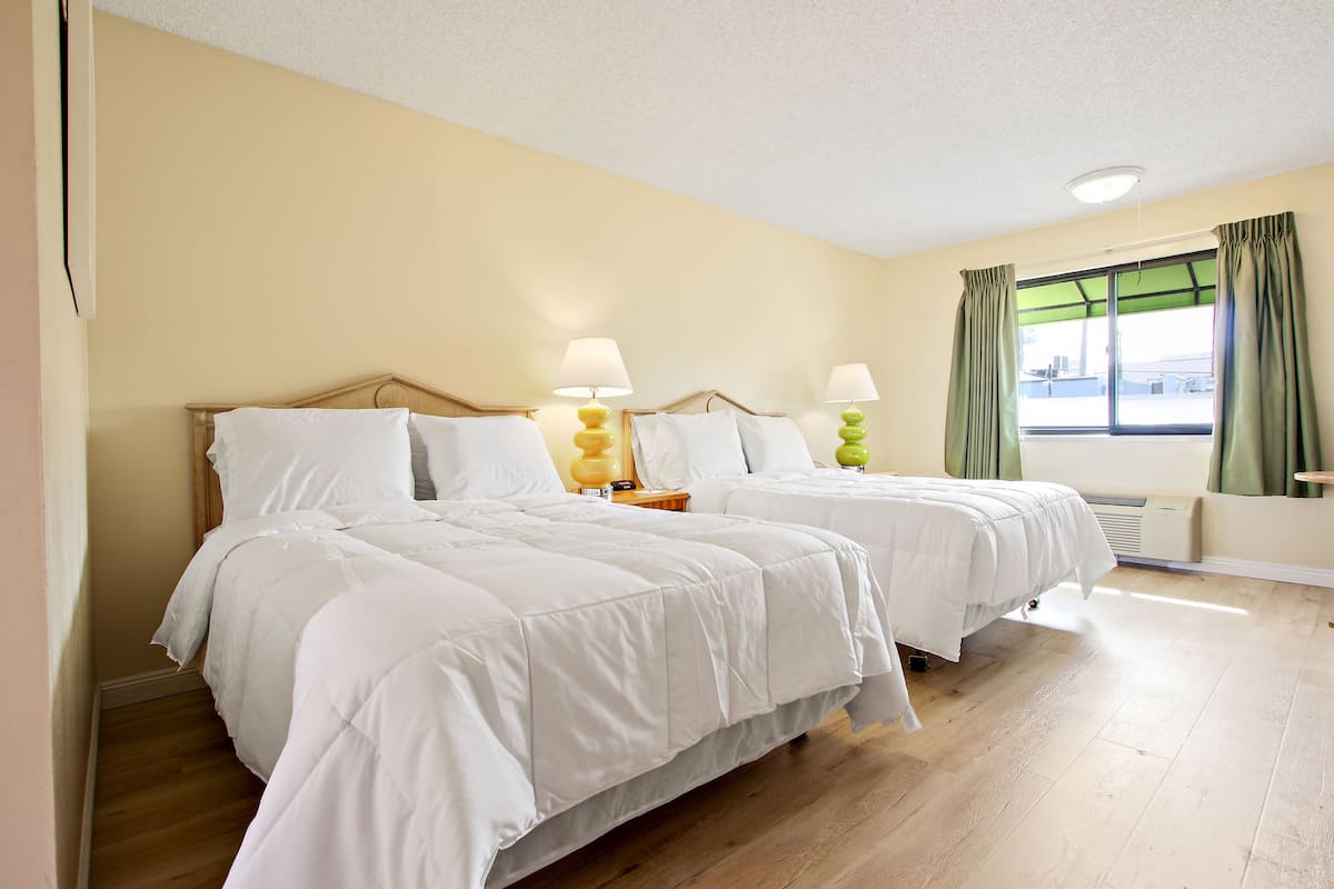 A hotel room with two beds, a window with curtains, and a bedside lamp.