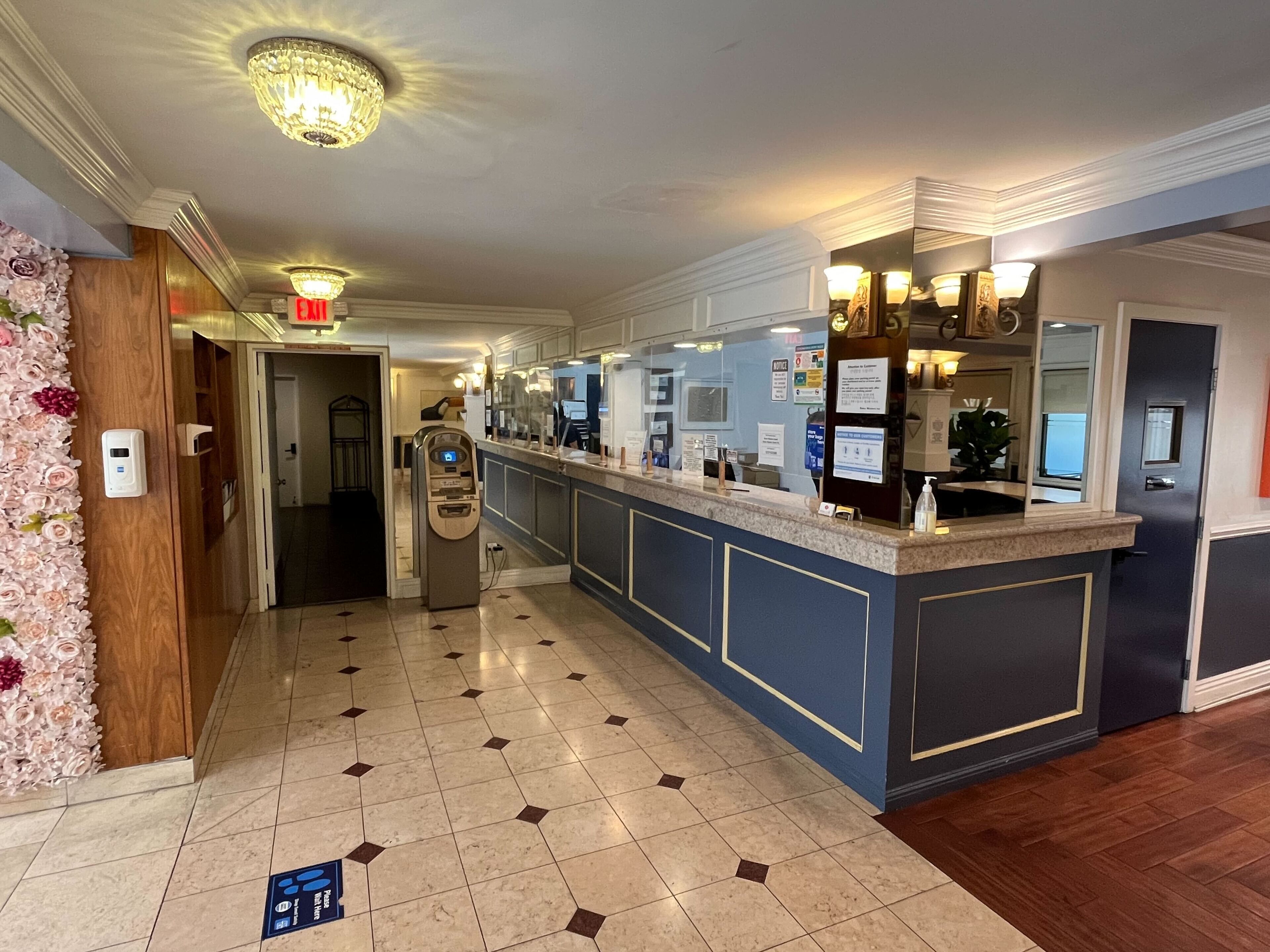Un hall d’accueil d’hôtel avec un sol carrelé en marbre, un comptoir d’accueil, un kiosque en libre-service et un lustre.