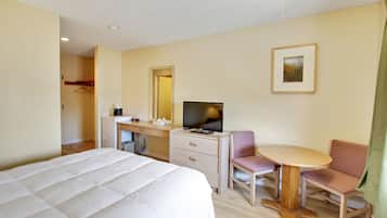A hotel room with a bed, a desk with a television, a chair, and a small table.