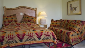 Une pièce avec un lit et un canapé, tous deux recouverts de couvertures à motifs. Il y a une lampe sur une table de chevet et un tableau encadré au mur.