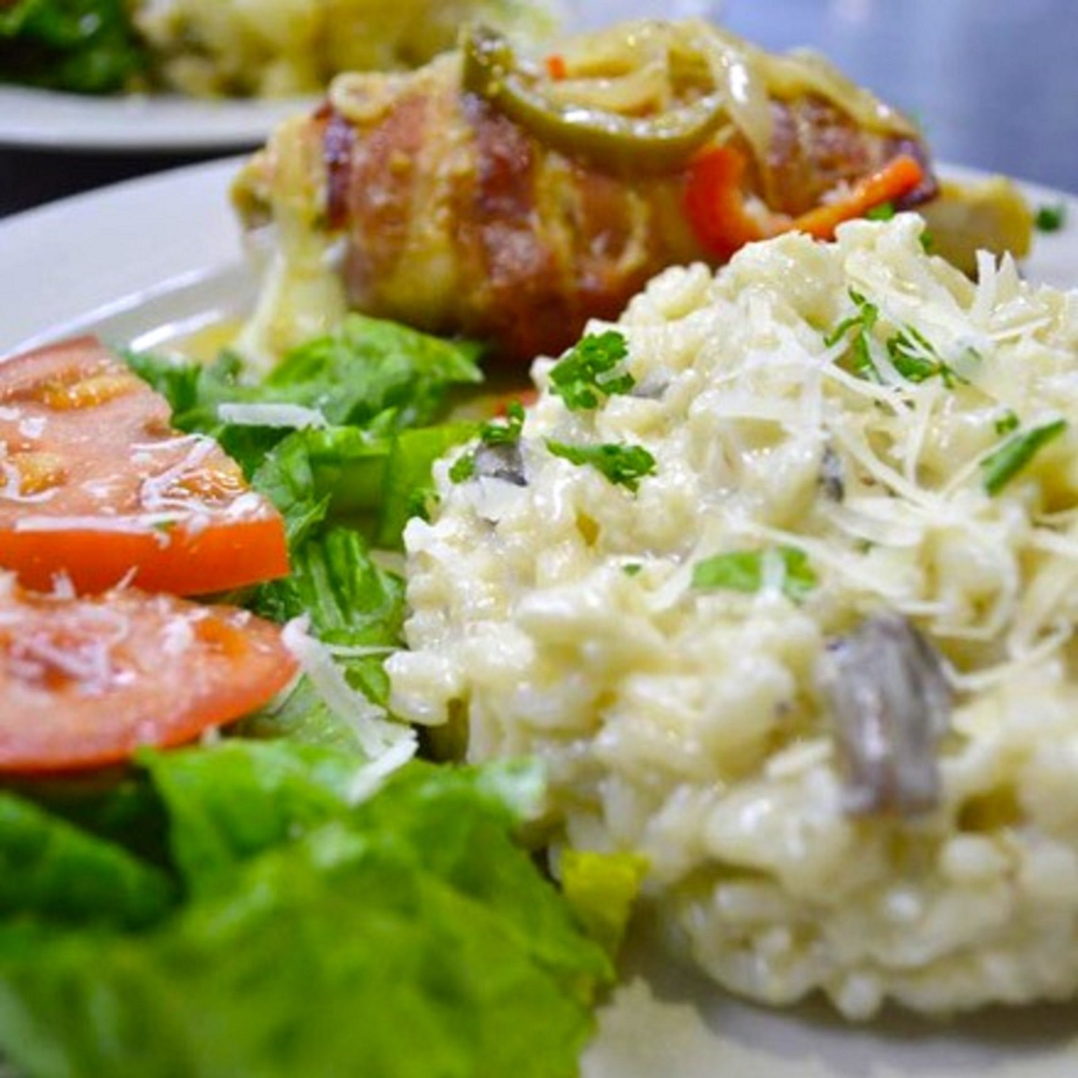 A plate with a salad, a slice of tomato, and a creamy dish with shredded cheese.