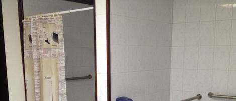 A bathroom with a toilet, a hand dryer, a trash bin, and a shower curtain.