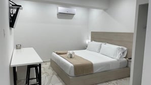 A single-bed room with a wooden headboard, a bedside table, and a small desk with a chair. - Arecibo Inn (Arecibo)