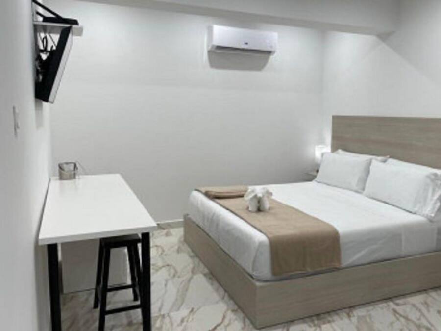Habitación individual con una cama de madera, cabecera de madera, una mesita de noche y un escritorio pequeño con una silla.