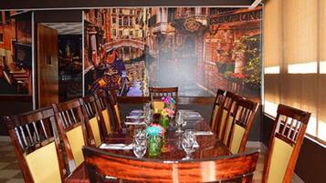 Un comedor con un amplio mural de un paisaje urbano, una mesa redonda con sillas y un jarrón con flores.