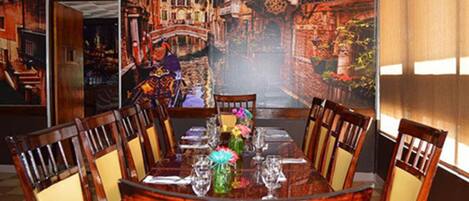 Un comedor con un amplio mural de un paisaje urbano, una mesa redonda con sillas y un jarrón con flores.