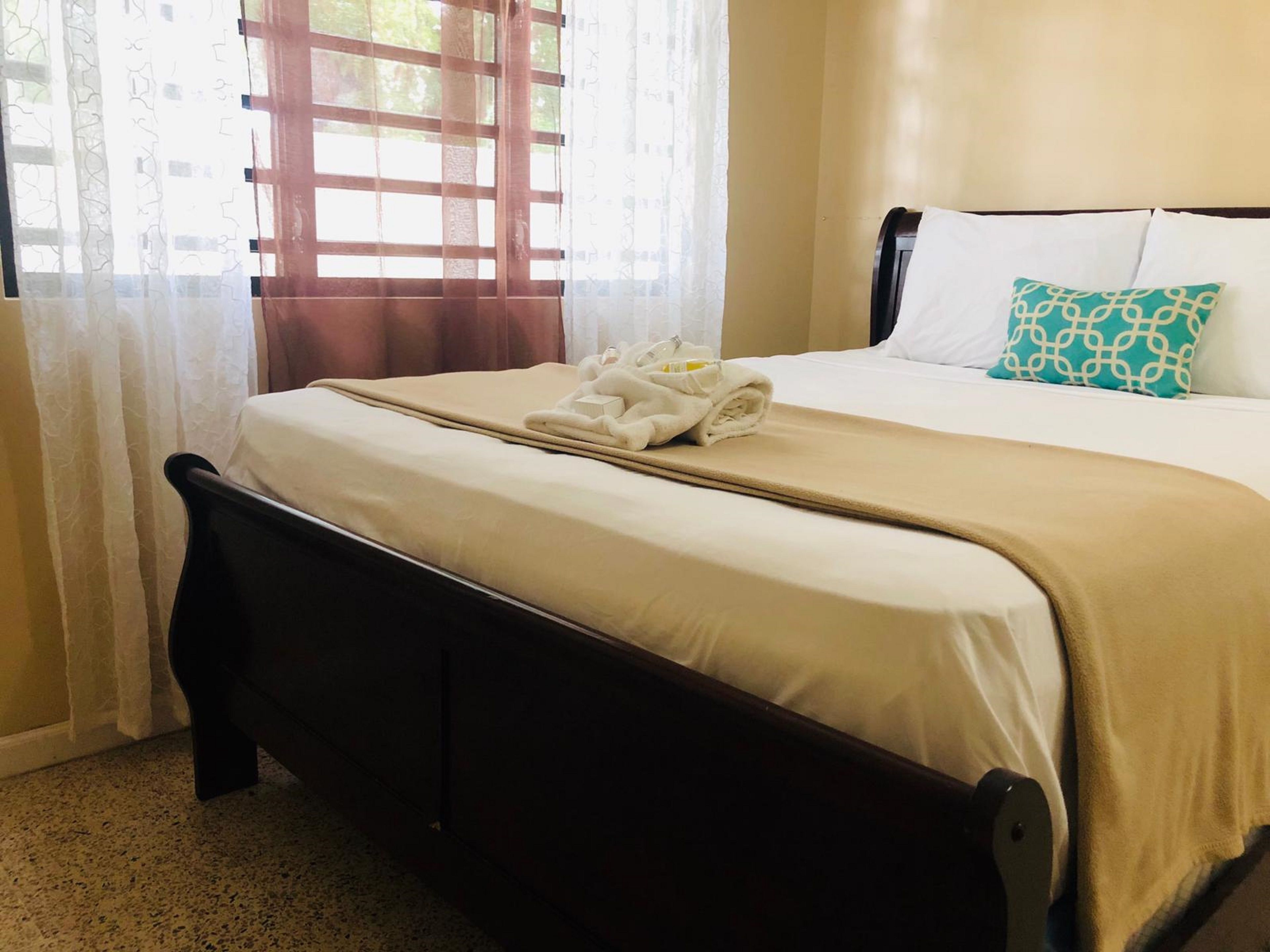 Una cama bien hecha con una colcha color beige, una almohada blanca y una almohada estampada.