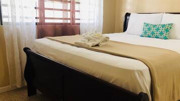 Una cama bien hecha con una colcha color beige, una almohada blanca y una almohada estampada.