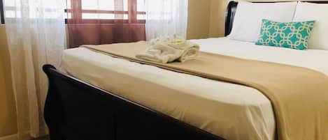 A neatly made bed with a beige bedspread, a white pillow, and a patterned pillow.