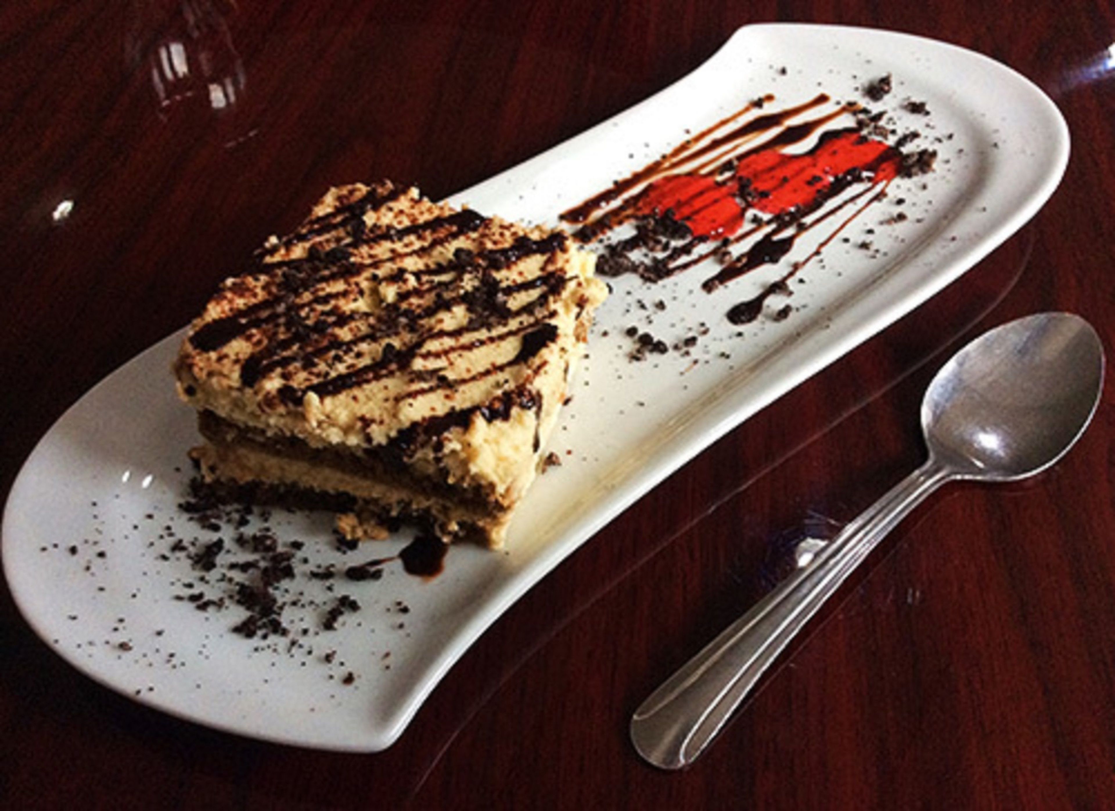 Une part d’un dessert à plusieurs couches, présentée sur une assiette blanche, nappée de chocolat et accompagnée d’une cuillère.