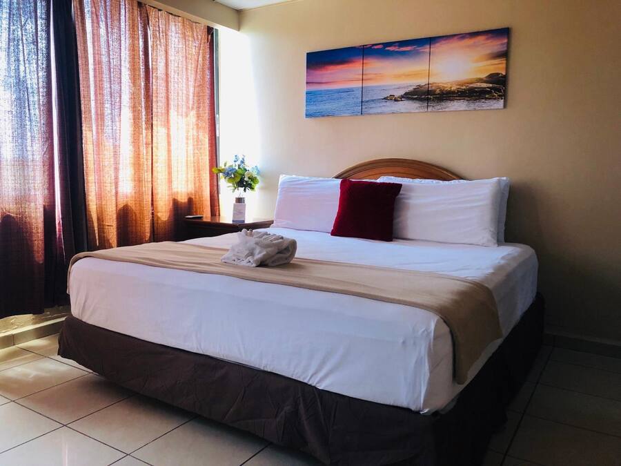 A neatly made bed with white and beige linens, a red pillow, and a folded towel on the bed.