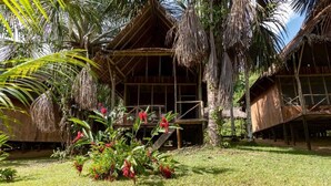A thatched-roof bungalow with a wooden deck and a small garden with red flowers.