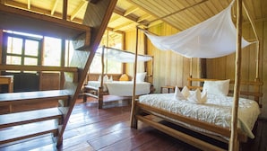 A traditional wooden room with four beds, each with a canopy. The room has a wooden floor and walls, and large windows allowing natural light.