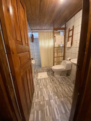 A narrow bathroom with a wooden door, a toilet, a sink, and a shower area. - Pacaya Samiria Amazon Lodge (Parinari)