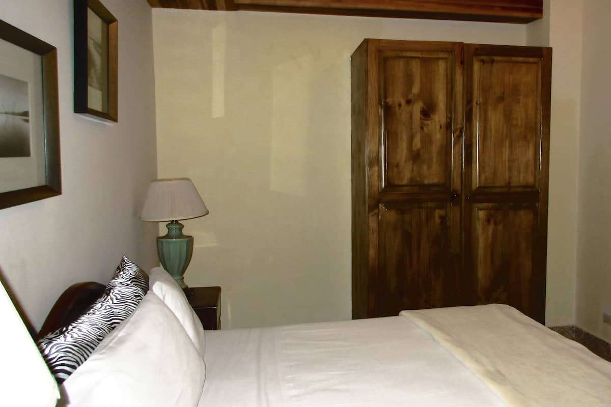 A bedroom with a bed, a wooden wardrobe, a lamp, and a framed picture on the wall.