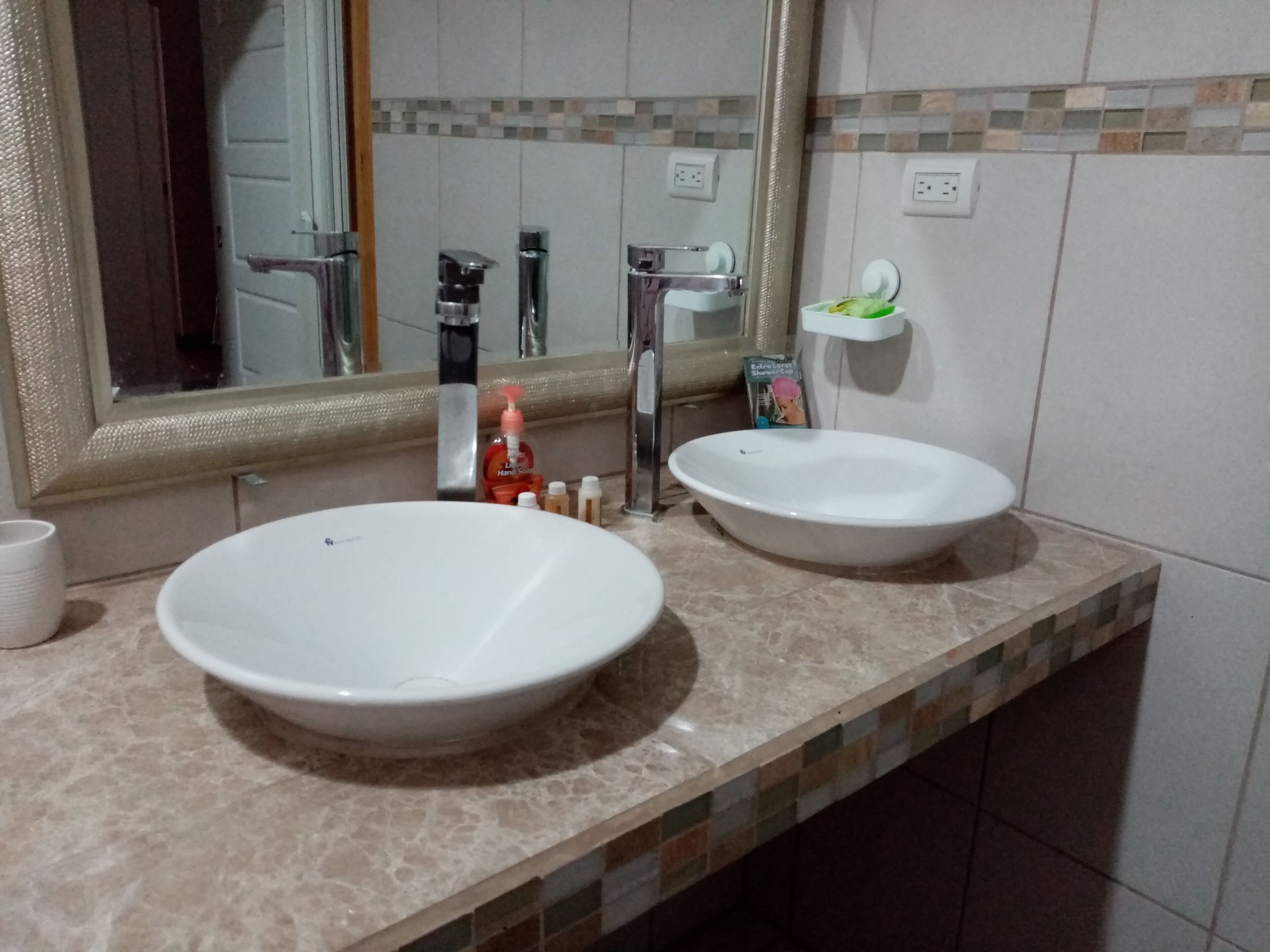 Une salle de bain avec deux lavabos blancs, un grand miroir et un mur recouvert de carreaux.