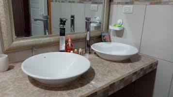 Une salle de bain avec deux lavabos blancs, un grand miroir et un mur recouvert de carreaux.
