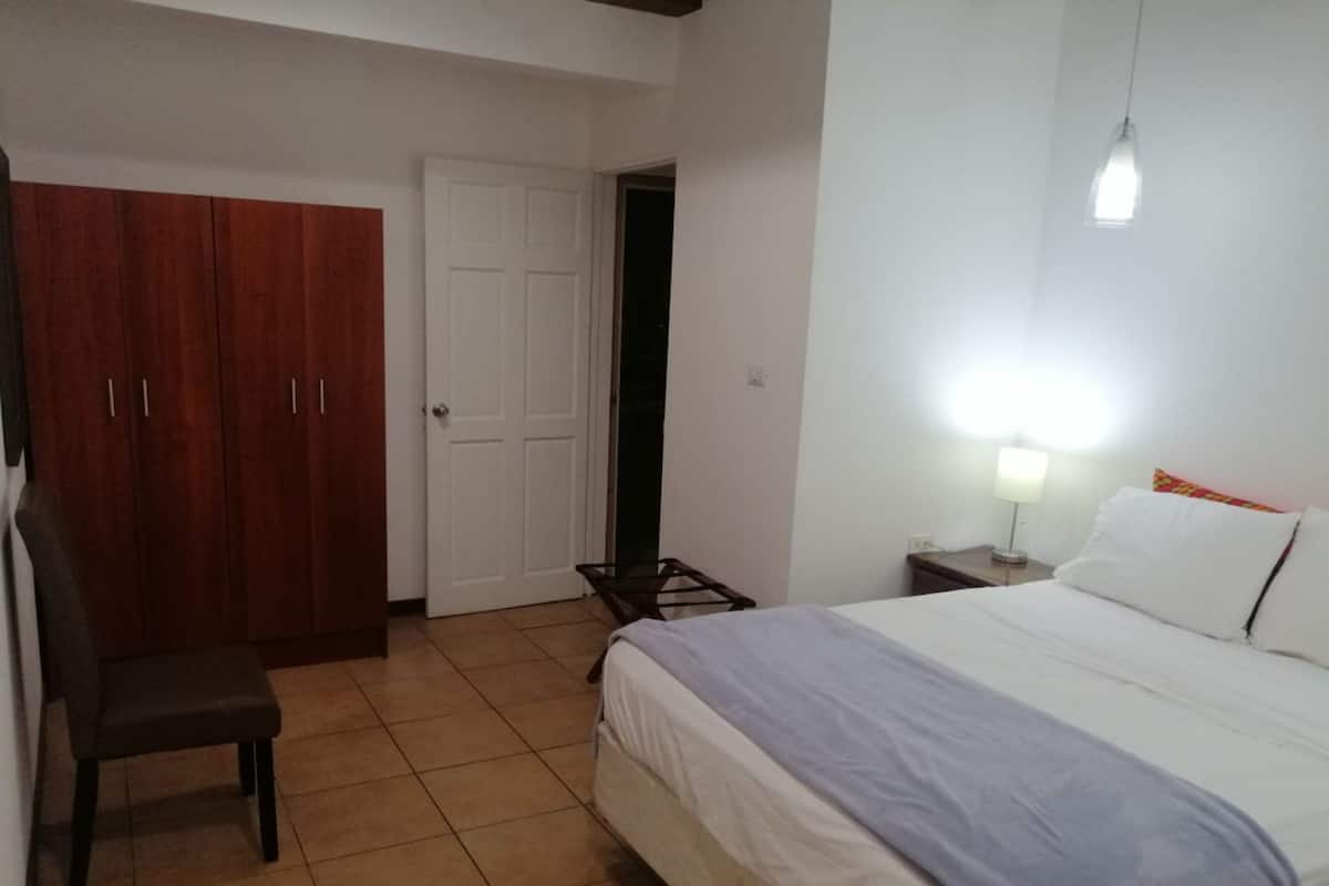 A bedroom with a bed, a chair, a wardrobe, and a door.