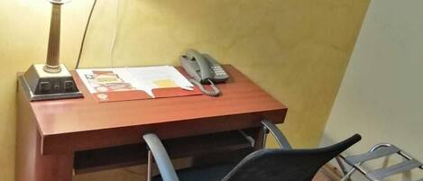 A small office space with a desk, chair, lamp, framed picture, and a telephone.
