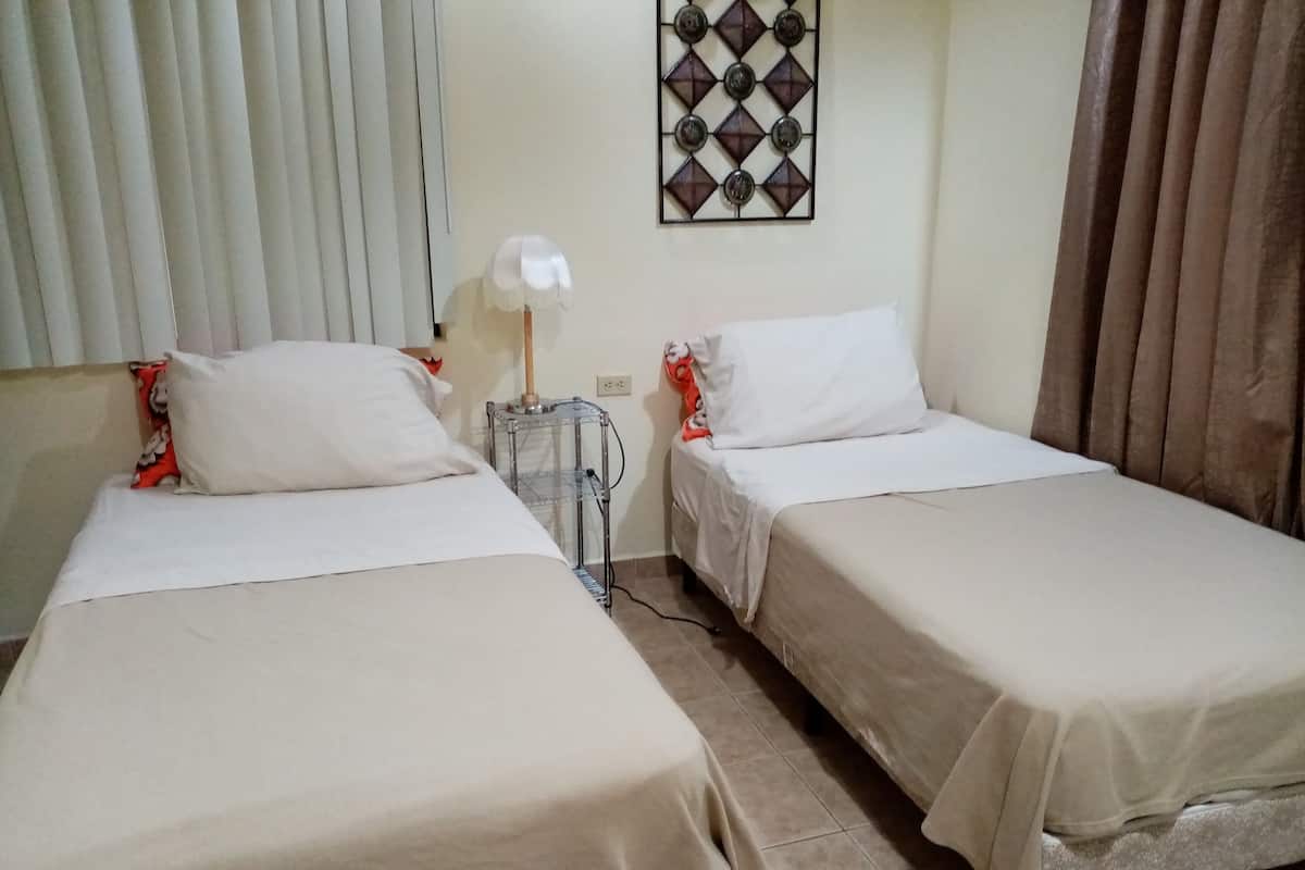 A room with two single beds, a small table with a lamp, and a decorative wall piece.