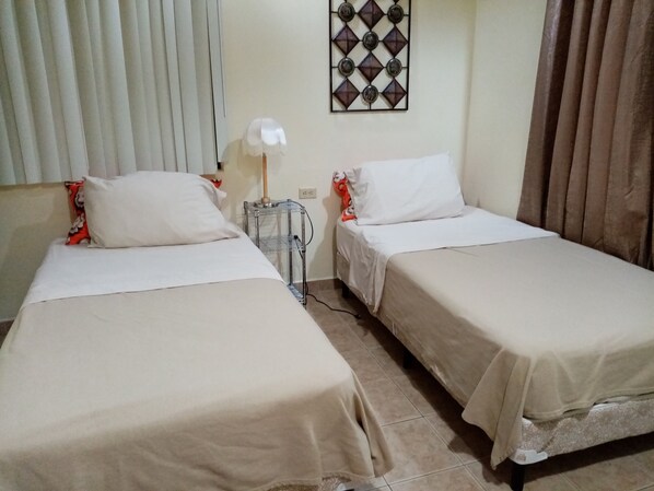 A room with two single beds, a small table with a lamp, and a decorative wall piece. - Apartotel Don Francisco (San Rafael)