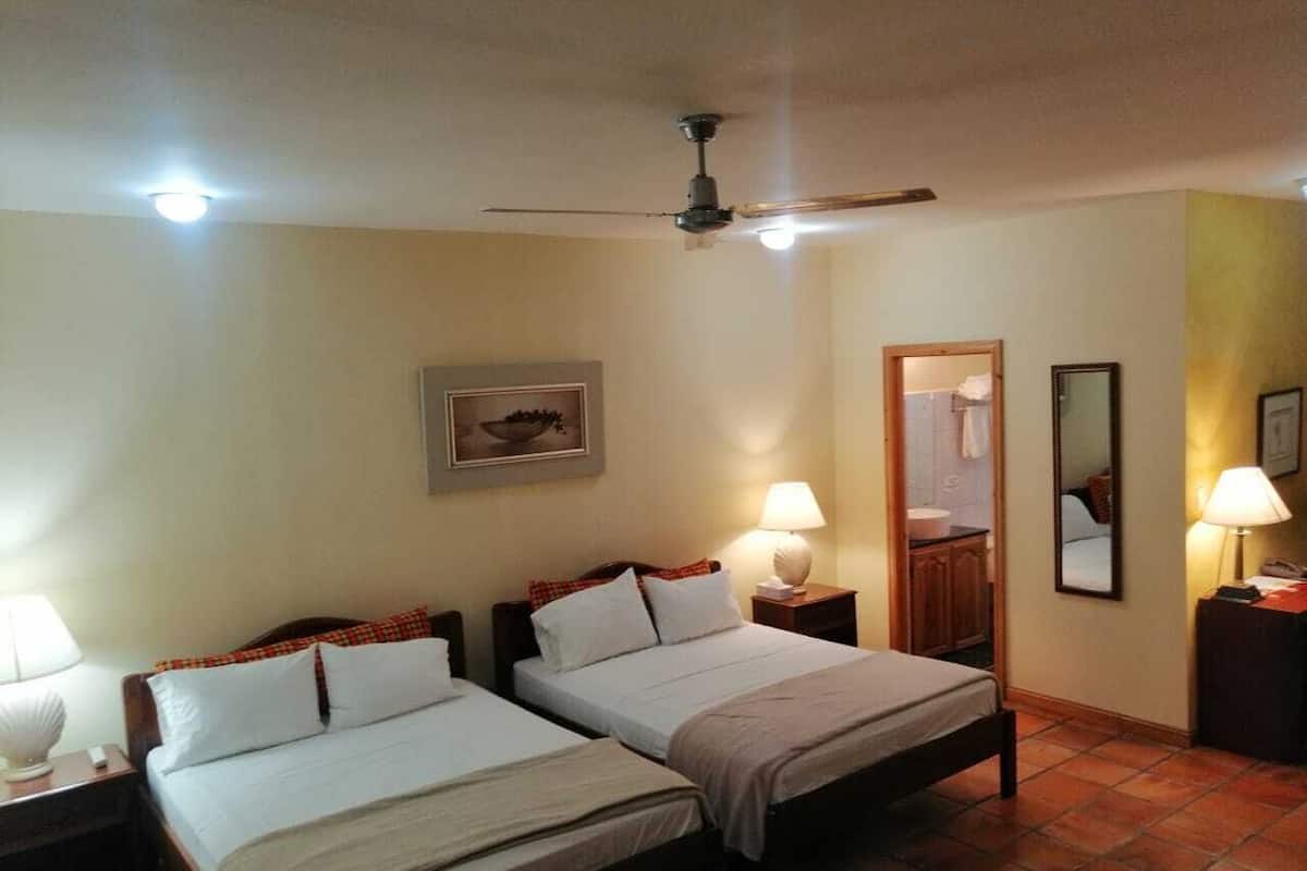 A hotel room with two beds, a ceiling fan, and a bathroom visible through an open door.