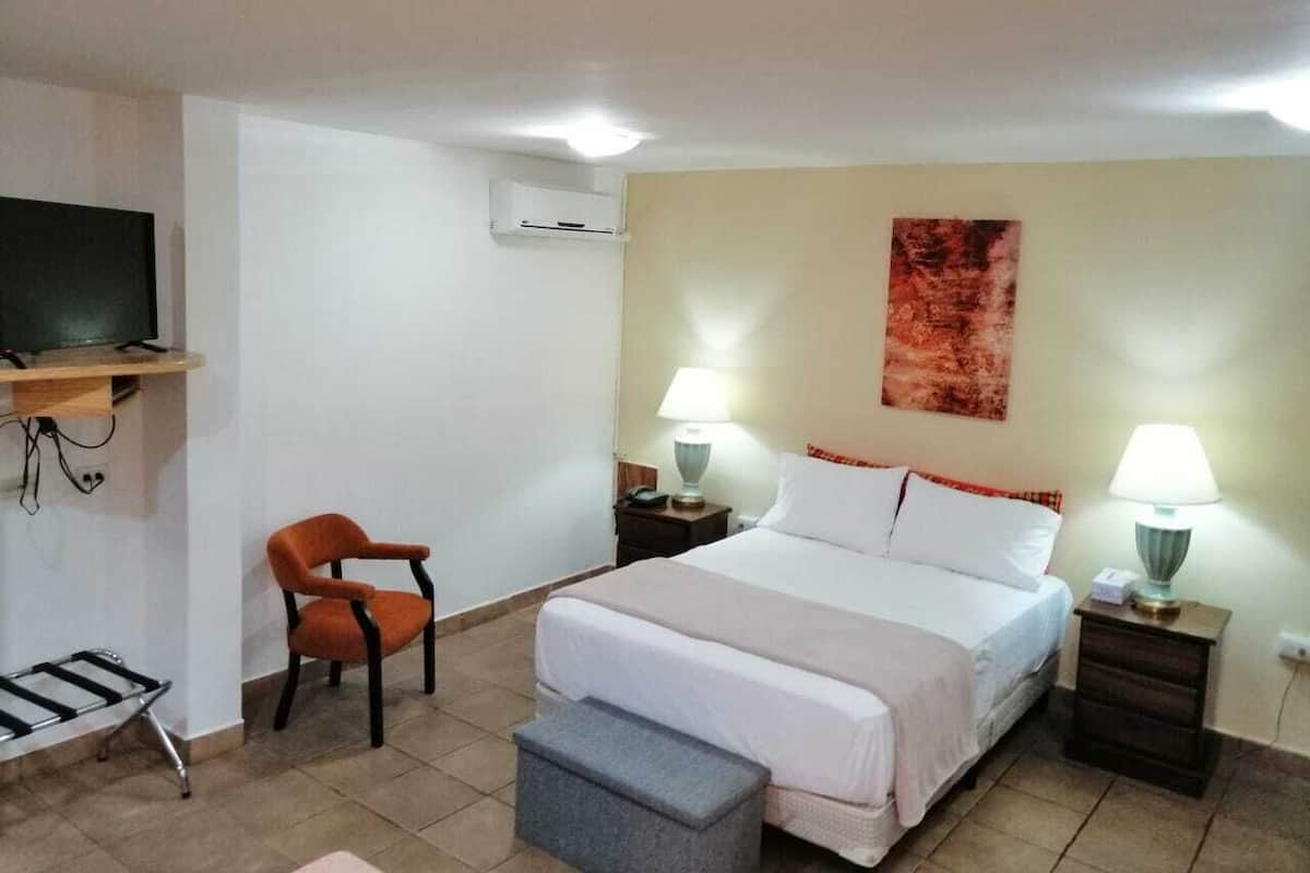 A hotel room with a bed, two bedside tables with lamps, a chair, a TV mounted on the wall, and a painting on the wall.