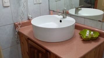 A bathroom with a white sink, a mirror, and two hair dryers on the wall.