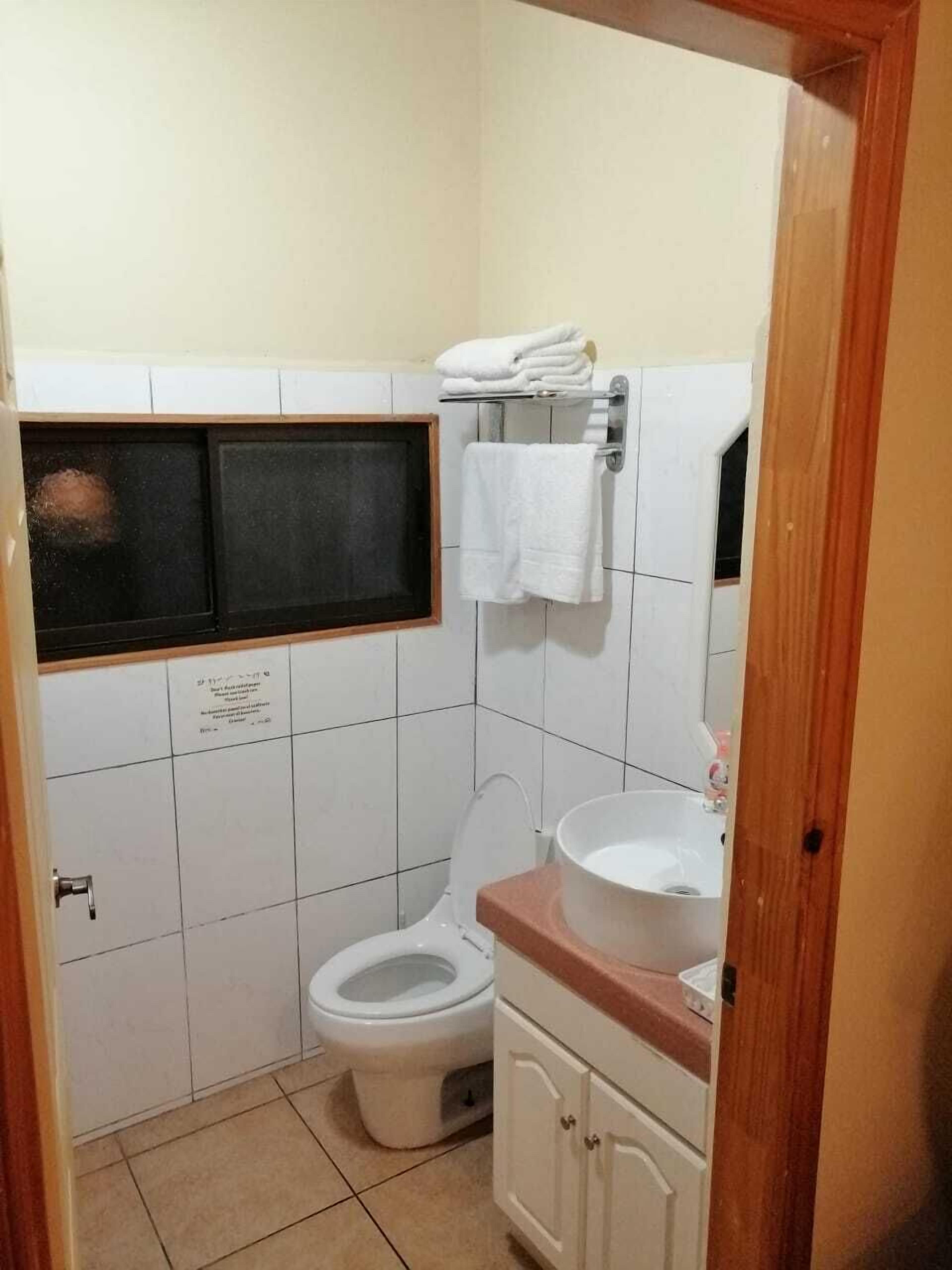 A small, clean bathroom with a toilet, sink, and a window above the toilet.