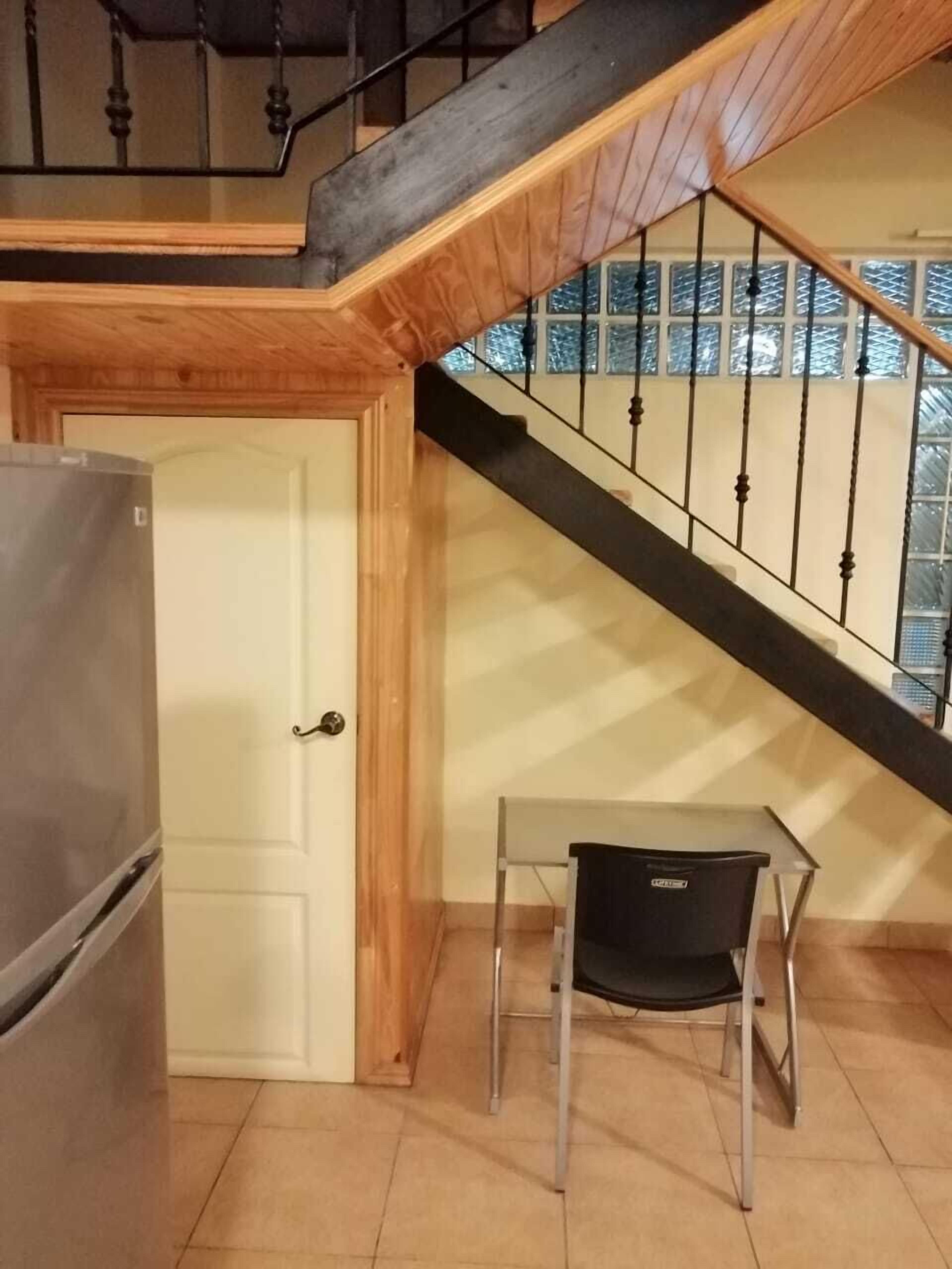 Una cocina con refrigerador, una puerta de madera y una escalera con barandilla de metal.