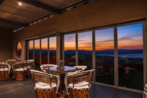 Ein Essbereich mit Korbstühlen und einem Tisch, große Fenster mit Sonnenuntergangsblick und ein runder Spiegel an der Wand.