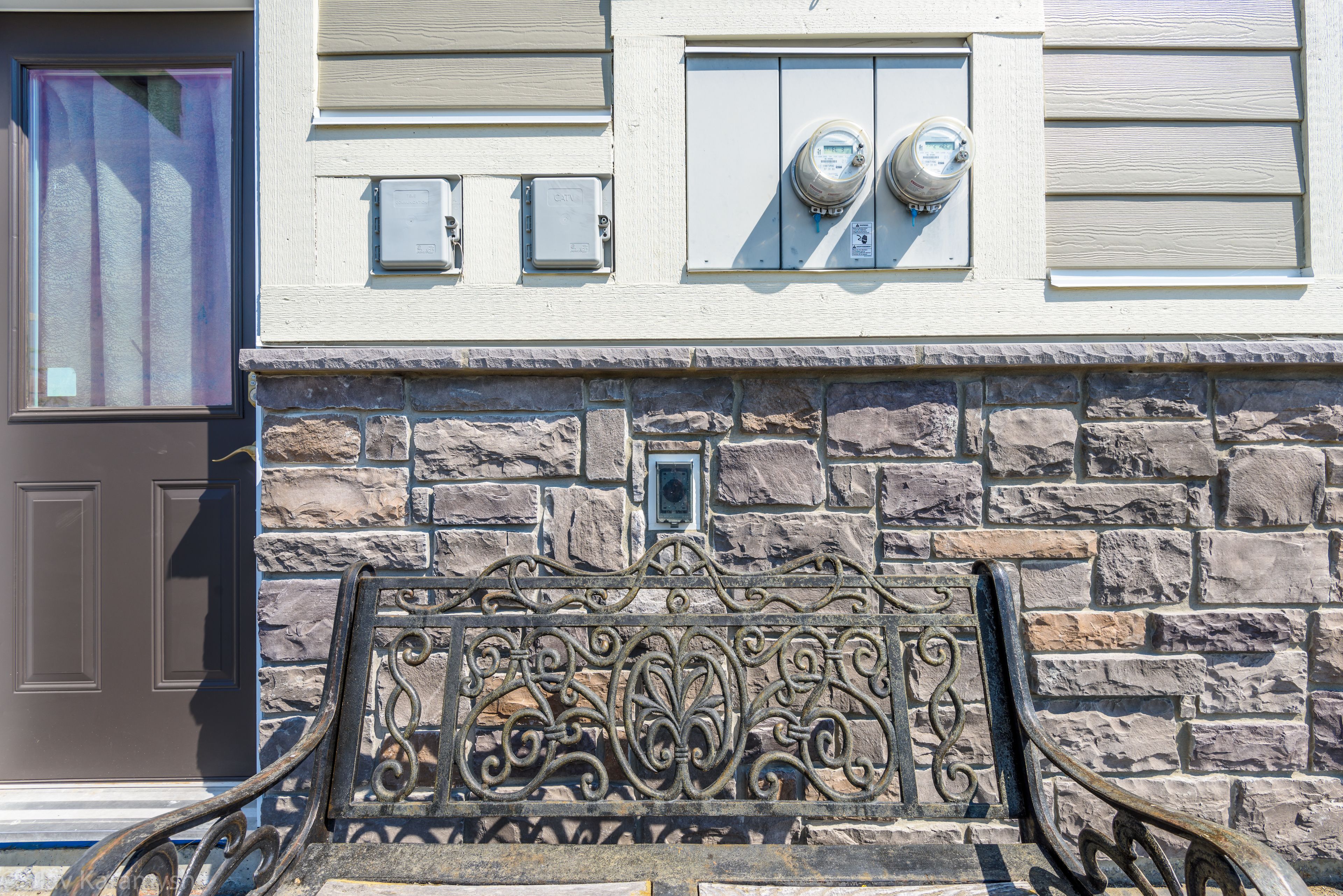 A stone facade with a metal decorative gate, a door with a purple tint, and utility meters on the wall.