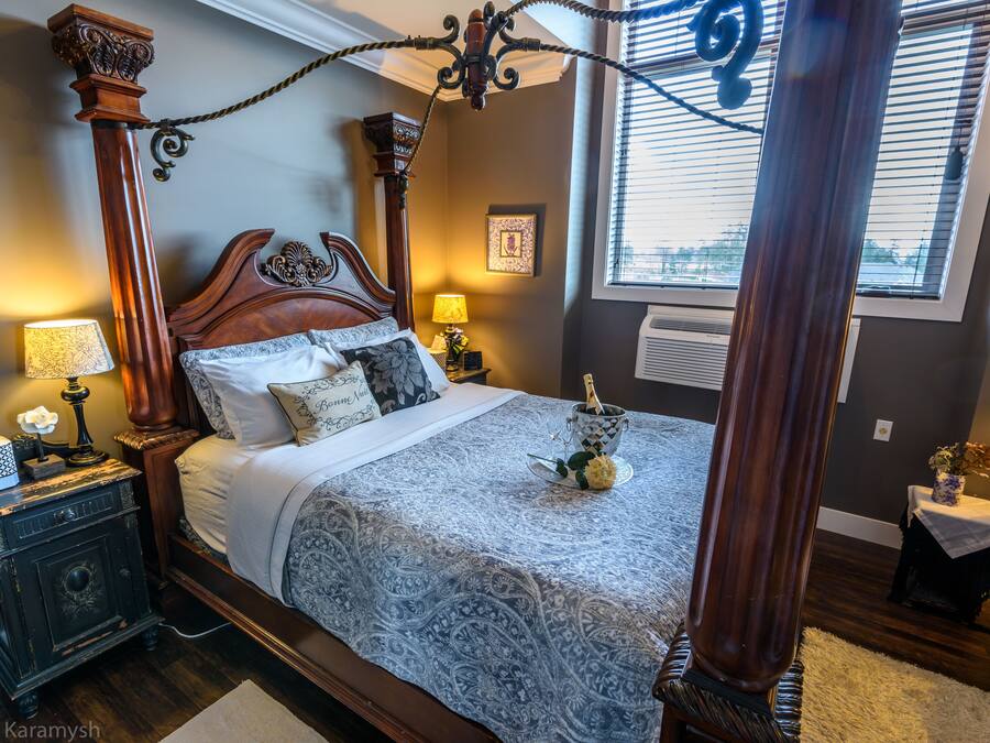 A four-poster bed with a canopy, a nightstand with a lamp, and a vase with flowers on the side table.