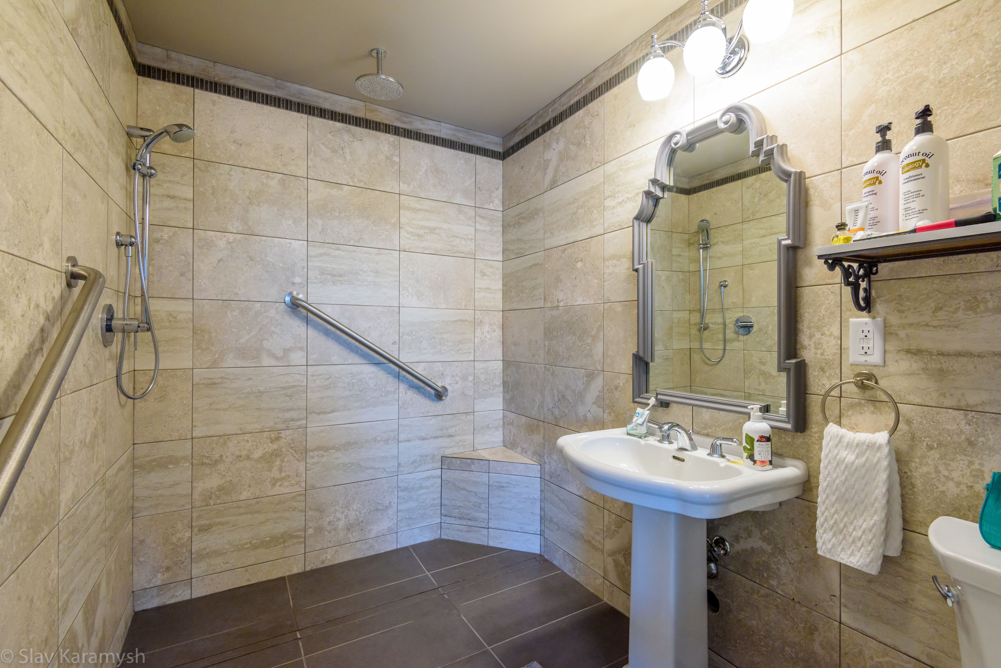 A bathroom with a shower, a sink, a mirror, and a handrail.
