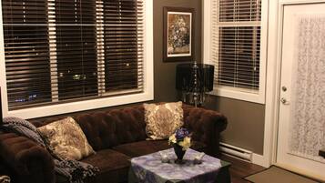 A living room with a brown sofa, two decorative pillows, a small table with a vase of flowers, and a framed picture on the wall.