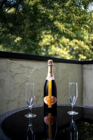 Een fles champagne op een ronde tafel met twee lege glazen, voor een achtergrond van groen.