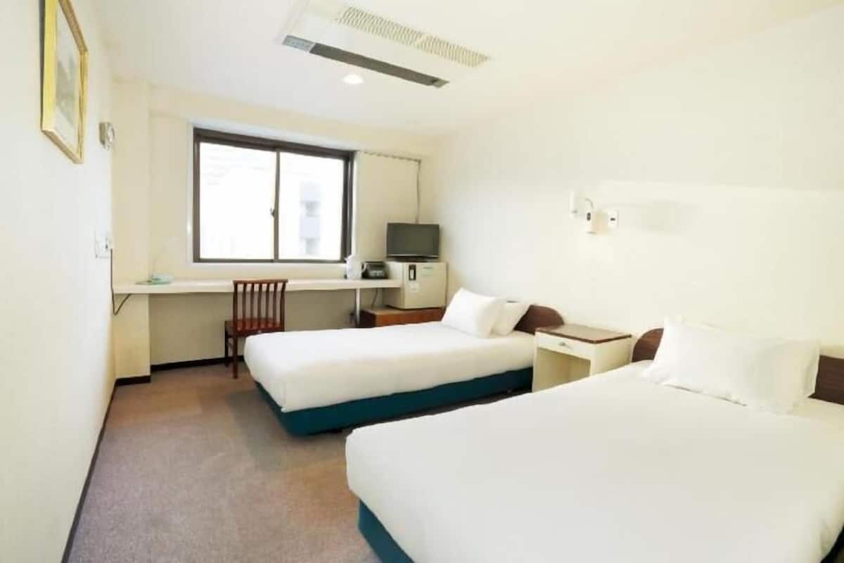A hotel room with two beds, a desk, a chair, a television, and a window.